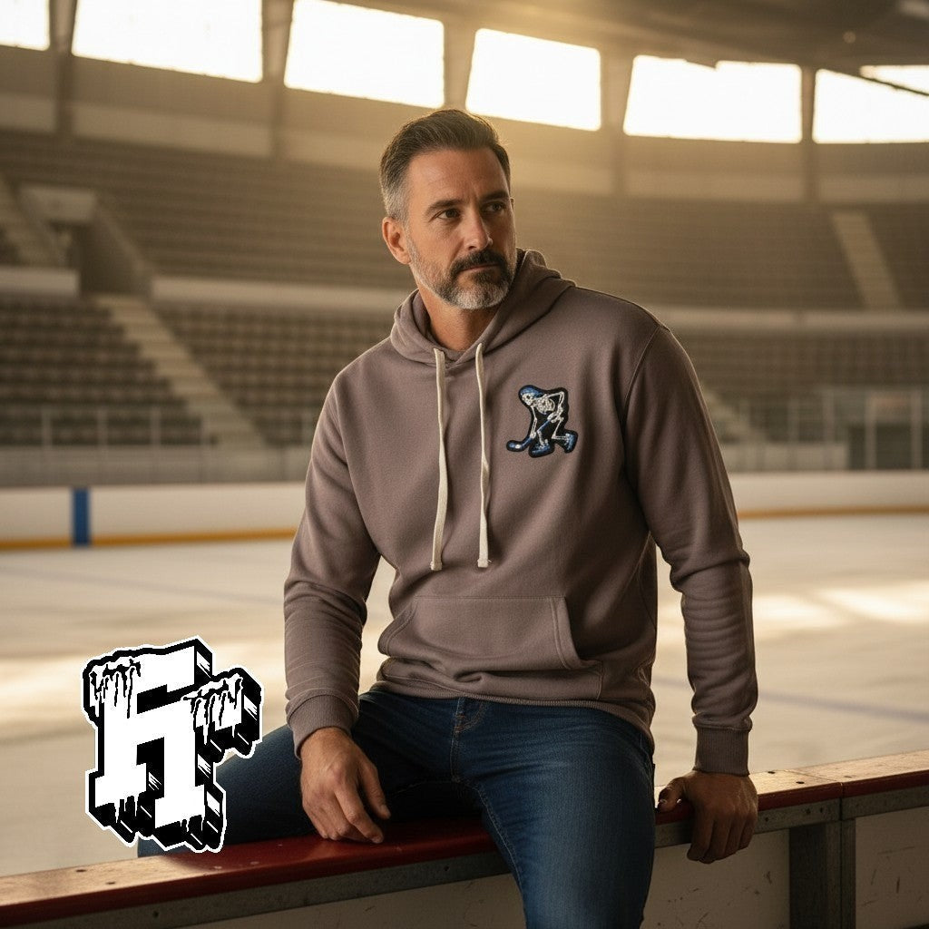 Frozen Threads Clothing taupe unisex hoodie with a Skelly hockey patch on the chest, jersey-lined hood, and front pouch pocket.
